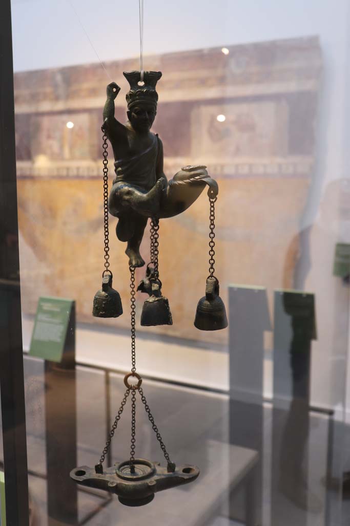 I.6.3 Pompeii. February 2021. 
Lamp with statuette of a satyr with a phallus from which small bells hang, on display in Antiquarium at VIII.1.4.
Photo courtesy of Fabien Bièvre-Perrin (CC BY-NC-SA).
