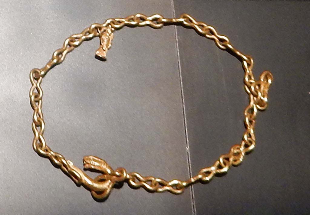 1.10.7 Pompeii, June 2019. 
Heavy gold chain with figure-of-eight links, snake head fastening and pendant featuring a statuette of Isis Fortuna, holding a rudder and cornucopia.
This was one of the jewels found in the atrium and in the tablinum.
On display in Palestra exhibition of jewellery entitled Vanity, storie di gioielli dalle Cicladi a Pompei, from 10th May 2019 to 5th August 2019.
SAP inventory number 5413. Photo courtesy of Buzz Ferebee.
See Guzzo, P.G. ed. (2003): Tales from an eruption  (Civale, A: The House of the Craftsman). Milan, Electa; (p.140-42)

