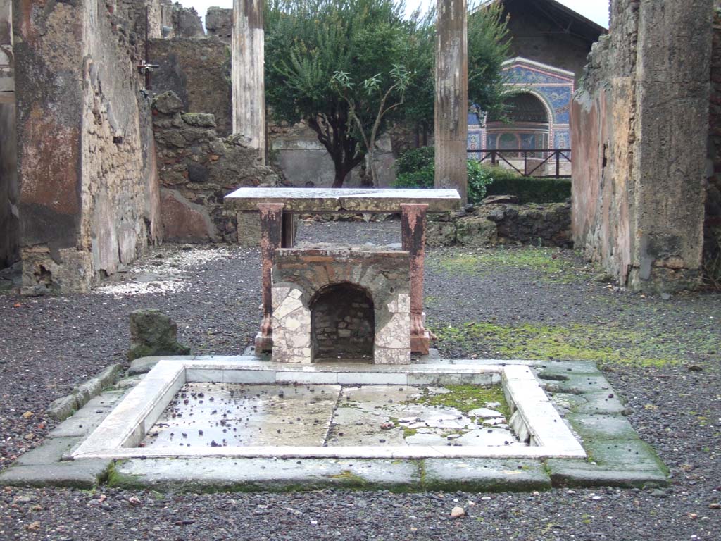 VI.14.43 Pompeii. December 2005. Room 1, impluvium in atrium, marble table and marble covered brick base or fountain.
According to Jashemski, unique so far at Pompeii, is the tiny mosaic fountain (about 0.50m high) in the atrium.
It had been built on the east edge of the impluvium, facing the entrance during the last years of the city. 
According to Sear, the front and bottom of the inside walls were lined with marble. 
Above this there was a “line of shells and then a zone of mosaic, in white, yellow, and blue, and above the mosaic another line of shells”.  
The head of the niche was covered with pumice and marine deposits.
See Jashemski, W. F., 1993. The Gardens of Pompeii, Volume II: Appendices. New York: Caratzas. (p.152)
