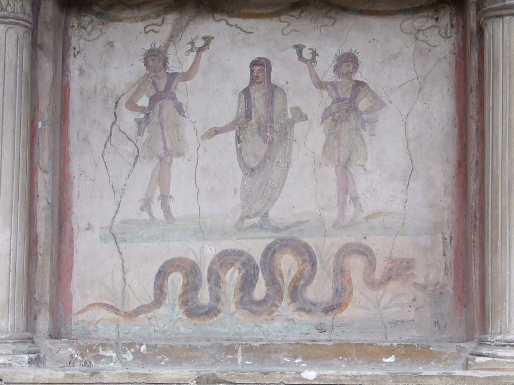 VI.15.1 Pompeii. December 2006. Household lararium in service area.
Painting of serpent, (Agathodemone), garlands and three figures.
The household gods (Lares) are either side of the guardian spirit (genius loci) of the house.
According to Boyce, this was located in VI.15.2.
He described it as one of the largest and finest lararia in Pompeii, consisting of a lararium painting within an aedicula.
The back wall within the aedicula is filled with a lararium painting on a white background.
In the centre stands the Genius, young and unbearded.
On each side of him stands a wreathed Lar, holding rhyton and situla.
The lower end of each rhyton has the form of a forepart of a goat.
In the lower zone of the same panel a crested and bearded serpent with brown back and yellow belly glides through plants towards the altar.
This painted square altar is shown at the right edge of the panel.
On the altar are an egg and some fruits.
Across the top of the panel are three garlands.
See Boyce G. K., 1937. Corpus of the Lararia of Pompeii. Rome: MAAR 14. (p.54, no.211, and Pl.30,2) 
See Giacobello, F., 2008. Larari Pompeiani: Iconografia e culto dei Lari in ambito domestico. Milano: LED Edizioni. (p.180-81)
See Fröhlich, T., 1991. Lararien und Fassadenbilder in den Vesuvstädten. Mainz: von Zabern. (p.279, L70).
