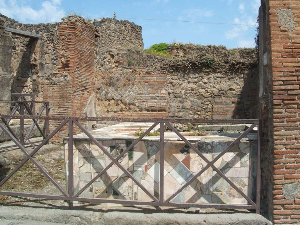 VII.2.33 Pompeii. May 2005. Looking north across entrance towards four-sided marble clad counter with seven built in urns.
To the left is the entrance at VII.2.32.
