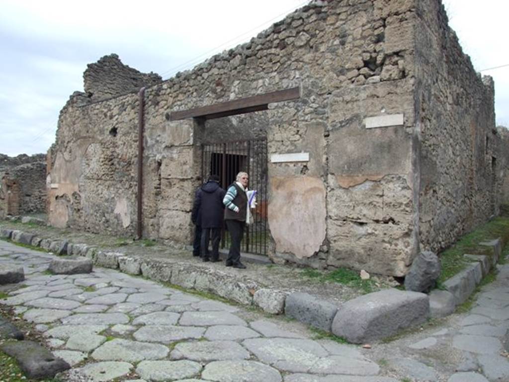IX.3.19 Pompeii. December 2007. Entrance doorway. According to Fiorelli, the shop communicated with a bakery, whose doorway was in the eastern roadway (IX.3.20).
It seemed to have been used for the sale of bread, and next to the entrance threshold of the doorway, was a shallow masonry parapet/podium for the mortar, on the other side were the marks for the staircase to the upper floor, under which was installed a storeroom/cupboard with three tiers of shelves. There were two tricliniums lit by windows, the first of which was decorated with two figures of Baccantes, one with thyrsus in hand and a basket on the head, the other carrying a thyrsus in the right hand and a vase in a basket in the left hand. There was also a head of Diana, facing forward, with quiver on the shoulder. A corridor that led to the bakery, had at its extremity the entrance doorway to an oecus/triclinium furnished by two windows, the one facing south towards another triclinium, the other looking out onto the adjacent bakery. The oecus/triclinium was decorated by two paintings alluding to the industry of the place. The first of these showed Ceres, sitting majestically enthroned, behind which was a standing Proserpina carrying a box, and to the right Triptolemus mounting onto the cart pulled by two serpents, scattering the grain on the ground received from the god; whilst the Earth, seen from the back, sitting between two small Genii, clutching the horn of plenty. The second painting showed Ariadne, laying by the sea on a bed of leaves with her head resting on a pillow, found by Bacchus who approached her led by a young Faun, followed by two Bacchantes, and two others that looked on from the top of a cliff.
See Pappalardo, U., 2001. La Descrizione di Pompei per Giuseppe Fiorelli (1875). Napoli: Massa Editore. (p.147)
and Fiorelli, G., (1875). Descrizione di Pompei, (p.397-8) 

