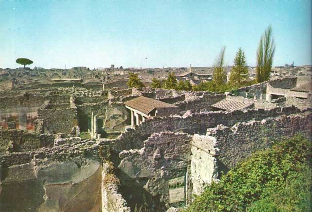 Looking north-west from Casina dell’Aquila to rear of entrance at IX.7.14, lower centre. 1968. 
On the left can be seen the west wall of the triclinium of IX.7.12.
The west wall of the garden can be seen behind the greenery, on the right of the doorway.
According to Boyce, against the west wall of the garden in a house only partially excavated, stood an aedicula.
It was built upon a square masonry base, the sides decorated with green plants painted on a white background.
Above the base, walls enclosed a niche. In front of the structure stood a small altar.
On the walls within the niche was the lararium painting. 
On the rear wall to the right of an altar, stood the Genius, pouring a libation upon the altar.
To the left of the same altar was a serpent, its head in stucco relief.
On each of the side walls were painted three figures, a plant, a Lar, and a man in a white garment.
The man held in his left hand an object, possibly a black cup, in his right hand was a patera.
See Boyce G. K., 1937. Corpus of the Lararia of Pompeii. Rome: MAAR 14. (p. 89, no. 445) 

