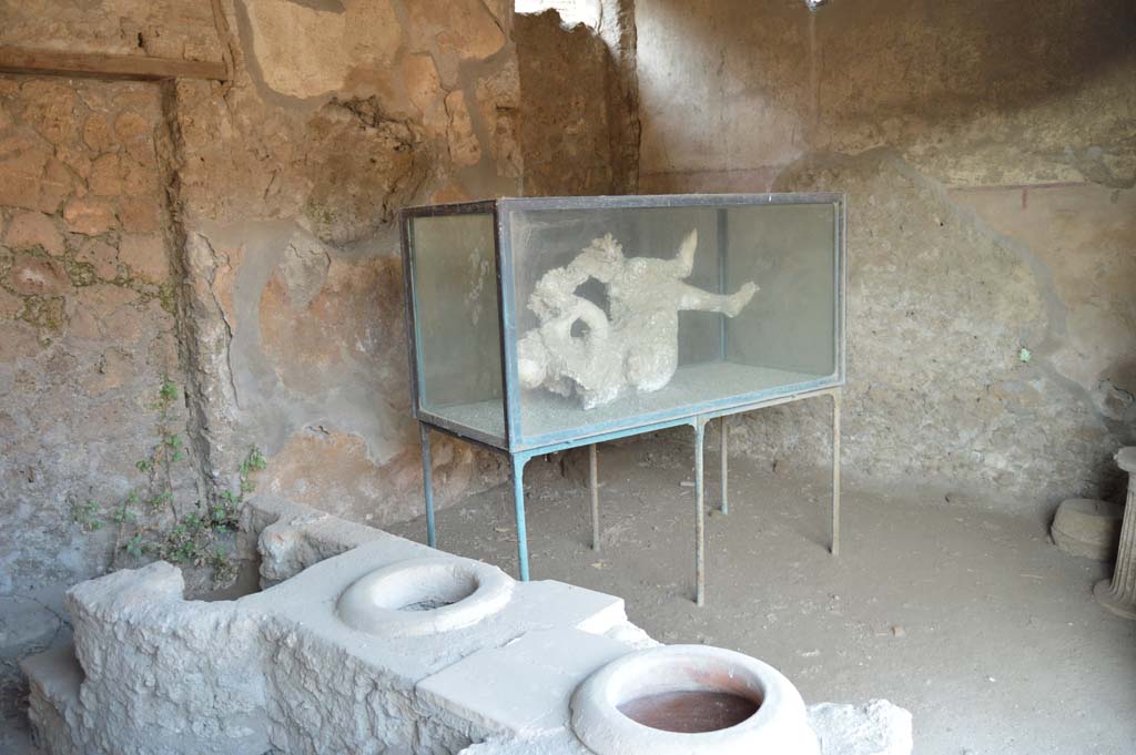 III.6.1 Pompeii. October 2017. Looking across east side of counter and hearth towards glass case with cast of victim 27 in north-east corner of bar-room.
Foto Taylor Lauritsen, ERC Grant 681269 DÉCOR.

