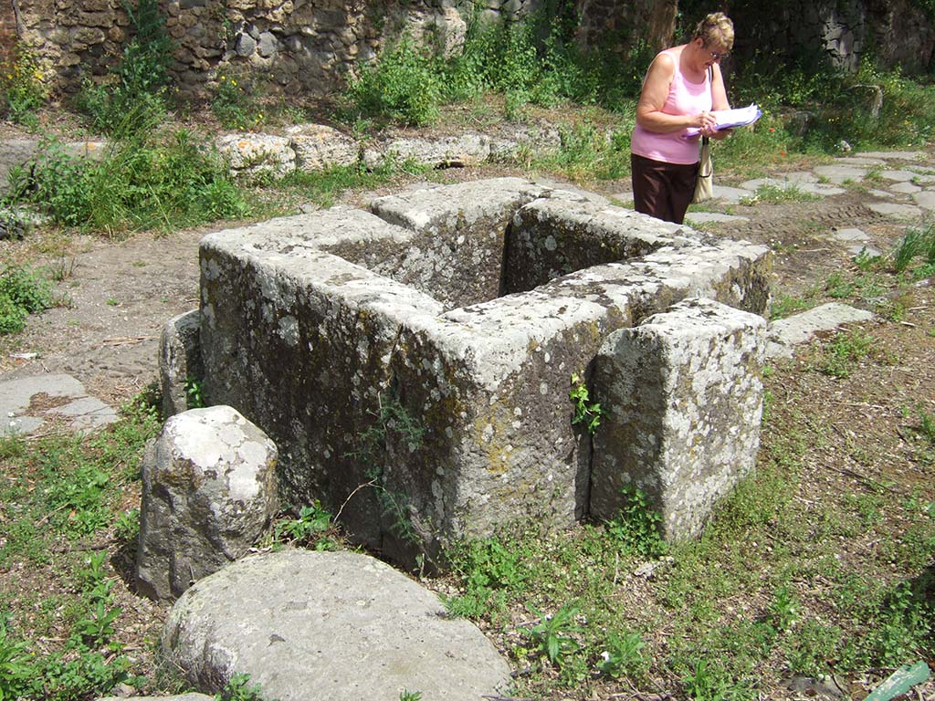 Via di Nola. May 2006. Looking north-east across street fountain on corner by III.11.1.
According to Eschebach, this fountain only had a basin and a fragment of the rear pilaster and no relief.
See Eschebach, H., 1983. Pompeii, Herculaneum, Stabiae; Bollettino dell’Associazione Internazionale Amici di Pompei 1, p. 12, Kat. Nr. 10. 
