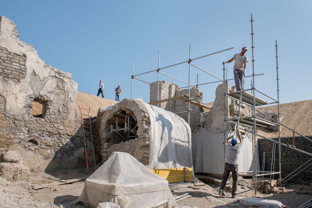 Pompeii Fountain at V.8 during excavation. 
Looking north-east from crossroads on Vicolo delle Nozze d’Argento, towards a small square/open area with water tower at rear, well/cistern with arched roof and fountain (covered). 
The gladiator fresco is on the back of the wall to the right of the water tower and behind the well/cistern.

Fontana di Pompei a V.8 durante lo scavo. Quadrivio con torre d'acqua sul retro, pozzo/cisterna con tetto ad arco e fontana (coperta). 
L'affresco gladiatore si trova sul retro della parete a destra della torre dell'acqua e dietro il pozzo/cisterna.

Photograph © Parco Archeologico di Pompei.
