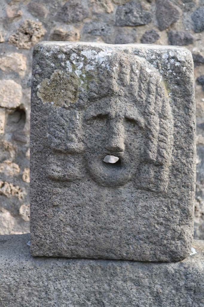 Fountain outside VII.11.5 on Vicolo della Maschera. December 2018. 
Relief of tragic mask. Photo courtesy of Aude Durand.
