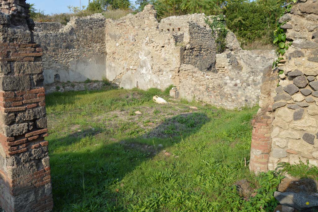 I.2.24 Pompeii. October 2017. Looking towards the north and east walls of the peristyle.  
Foto Taylor Lauritsen, ERC Grant 681269 DÉCOR.
According to Boyce –
In the east wall of the peristyle, above one of the beds of a masonry triclinium, is a niche, described by Fiorelli as a sacrario, more fully by Mau as 
“un aedicula, una base, cioè, con una piccola tavola, che sta in un specie di nicchia coperta a volta, e probabilmente conteneva un’idolo”. 
[an aedicula, a base, that is, with a small table, which is in a sort of vaulted niche, and probably contained an idol".]
There remains now only the solid base (0.40 by 0.32, h.0.65) and on the wall above it the marks left by a vaulted structure which rested on the base.
He quotes references – Bull. Inst., 1874, 262; Fiorelli, Descr., 47.      

