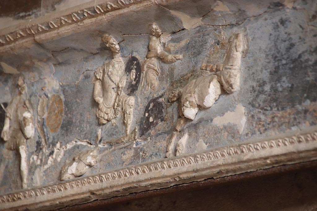 I.6.4 Pompeii. October 2024. Room 16. Hector is dragged behind a chariot.
Detail from frieze on west wall of sacellum towards south end. Photo courtesy of Klaus Heese.
