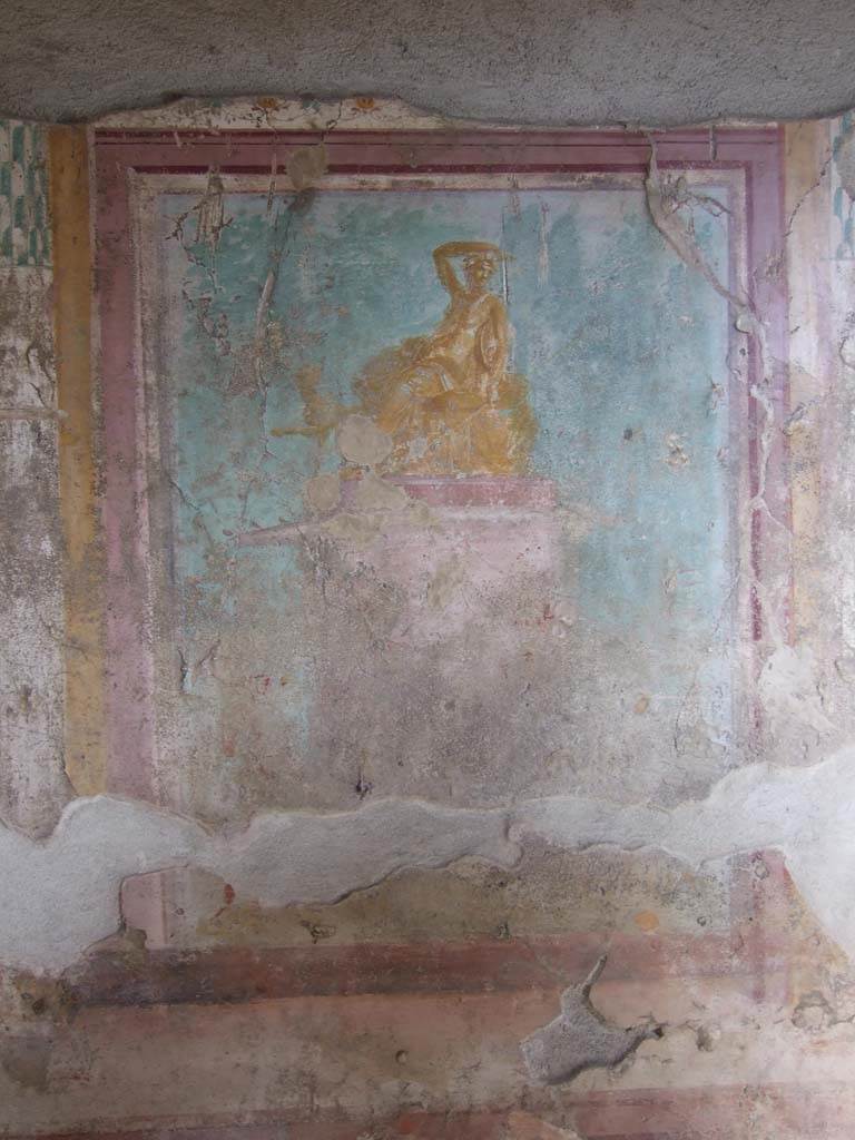 V.1.18 Pompeii. March 2009. East wall of exedra “y”.  
Wall painting of Dionysus (or Ariadne?) seated on a pedestal.
See Leach, E.W., 2004. The Social Life of Painting in Ancient Rome and on the Bay of Naples. Cambridge UK: Cambridge UP. (p.135).
According to NdS, it is Bacchus, seated, with his arm on his head and his panther at his feet.
The panther has turned its head towards Bacchus.
See Notizie degli Scavi di Antichità, 1876, p. 79.
Kuivalainen describes this as a composition of three (or four) figures. 
In the left corner, a naked male carries a sack or a wineskin in his left hand. In the middle stands a wreathed Silenus with several wineskins on the ground. (There may be a third figure between these two.)
The red pedestal with white details is decorated with garlands; on top of the pedestal, on a bench covered with a cloth and a thick pillow, reclines an effeminate youth; his body is golden yellow with reddish shades and white reflections; his right arm is raised on top of his head, turned left, wreathed and with two small horns; he holds a cantharus in his hand, in his left arm he has a thyrsus pointed downwards and a tympanum; he wears a thin cloak, which covers his legs, and a nebris tied over his left shoulder. 
Behind his knees peeks a panther, standing with his left foreleg raised. Trees are painted across the background.
Kuivalainen comments –
Bacchus is depicted as a gilded bronze statue. The effeminate features and small breasts are typical for a young Bacchus with horns, but the tympanum as his personal attribute is rare. The reference to the Anthesteria is theoretical, with wine skins as the only references, nor does the pictorial programme with its plethora of paintings in the room support this interpretation, as the paintings are rather linked to Bacchus and Venus.
See Kuivalainen, I., 2021. The Portrayal of Pompeian Bacchus. Commentationes Humanarum Litterarum 140. Helsinki: Finnish Society of Sciences and Letters, p.185.
(Note: in his Bibliography he quotes – Dilthey 1876, 311-313, (AdI): Effeminate Bacchus, with a similar statue found in Herculaneum (MANN 9276), a drinking contest in the Anthesteria festival in Athens.)
