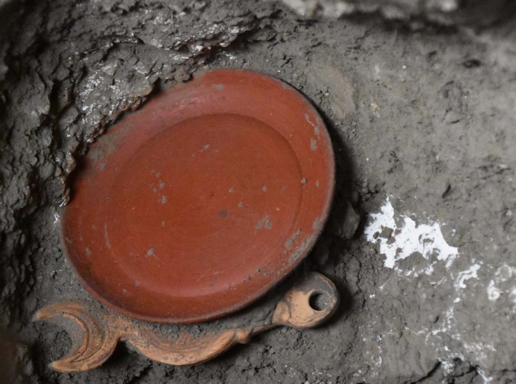 V.3.13 Pompeii. 2022. Room 3b, bedroom. Chest contents.
A small sigillata plate and a double-spouted lantern.
Un piattino in sigillata (tipo di ceramica romana fine da mensa) e una lucerna a doppio beccuccio’
Photograph © Parco Archeologico di Pompei.


