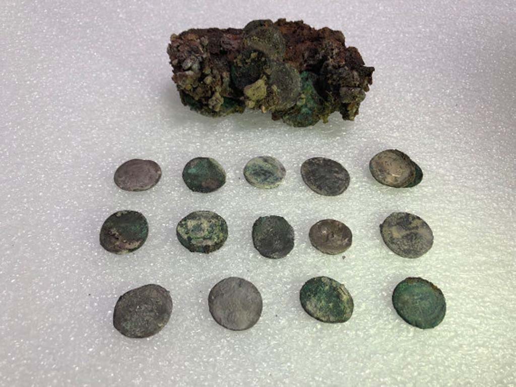 Regio V Pompeii. 2018. Leather pouch containing coins found under Pompeii skeleton in the Vicolo dei Balconi.
At first examination of the money found with skeleton of victim there would seem to be at least 20 silver denarii and two bronze asses for a nominal value of eighty sesterces and a half. 
Such a quantity of coins could at that time ensure the maintenance of a three-person family for 14, 16 days. 
The coins have very varied chronology. 
It was possible to examine 15 coins, for the main part Republican, starting from the Mid-second century B.C. 
One of the later Republican coins is a legionary denarius of Mark Antony, common in Pompeii, with the indication of the XXI Legion. 
Among the few Imperial coins identified, a probable denarius of Octavian and two denarii of Vespasian.

Borsa di cuoio contenente monete trovate sotto lo scheletro di Pompei nel Vicolo dei Balconi.
Al primo esame delle monete trovato con lo scheletro della vittima sembrerebbero esserci almeno 20 denari d'argento e due as di bronzo per un valore nominale di ottanta sesterzi e mezzo.
Una tale quantit di monete potrebbe quindi garantire il mantenimento di una famiglia di tre persone per 14, 16 giorni.
Le monete hanno una cronologia molto varia.
Fu possibile esaminare 15 monete, per lo pi repubblicane, a partire dalla met del II secolo a.C.
Una delle monete repubblicane pi tardi  un denario legionario di Marco Antonio, comune a Pompei, con l'indicazione della XXI Legione.
Tra le poche monete imperiali identificate, un probabile denario di Ottaviano e due denari di Vespasiano.

Photograph  Parco Archeologico di Pompei.
