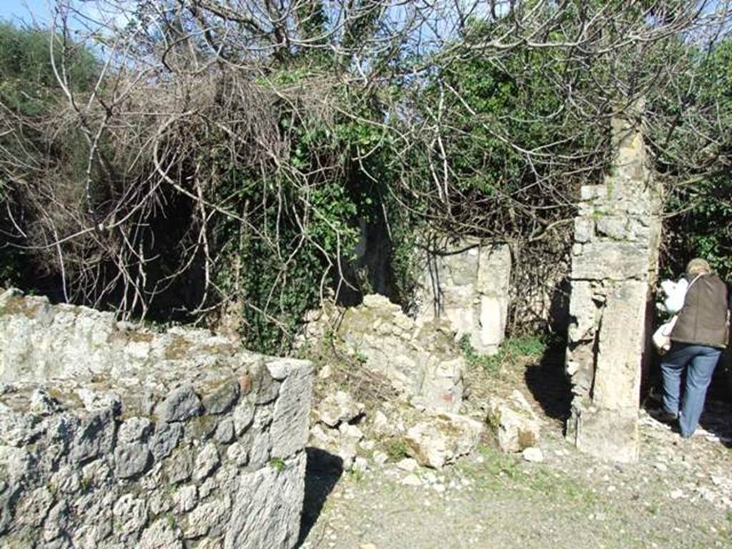 V.4.c Pompeii. March 2009. Ruined doorway of room F, cubiculum or rustic room in the north-east corner of atrium B. Looking east from restored wall of triclinium D, across room E, ala, towards to room F.  In the east wall of the ala, the doorway to rustic room F was found. It would have had a wooden threshold, a mortar floor, and white stucco on the walls. In the south wall, at a height of 0.95m from the ground, a small area was found with traces of shelving. See Notizie degli Scavi, 1905, (p.133).