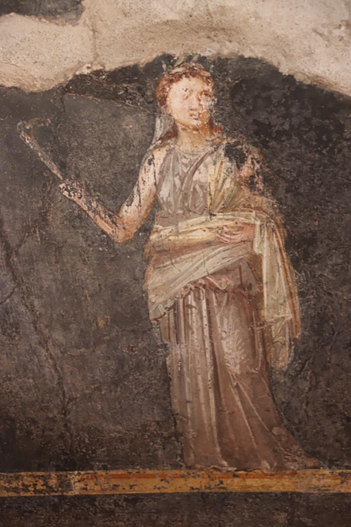 VI.15.1 Pompeii. October 2023. 
West wall at south end, painting in zoccolo of female figure or priestess holding implement of sacrifice.
Photo courtesy of Klaus Heese.

