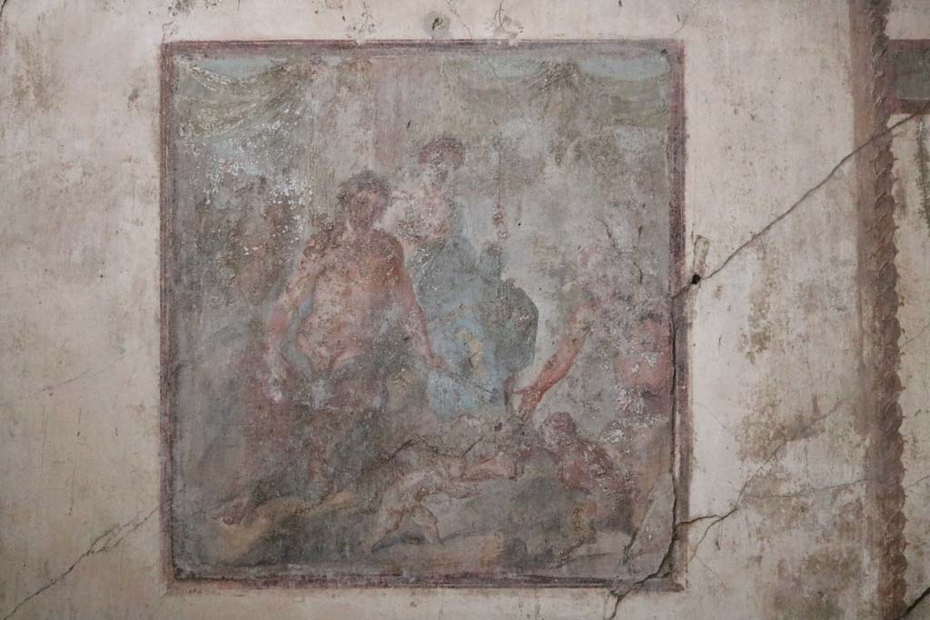 VI.15.1 Pompeii. December 2018.  
Central wall painting on south wall showing Dionysus and Ariadne, as well as the fight between Eros and Pan. Photo courtesy of Aude Durand.
Kuivalainen comments –
“A young half-naked Bacchus in the company of Ariadne, watching the fight about to begin, and Silenus already preparing to reward the victor with the palm leaf. The female figure’s dignified appearance suits Ariadne more than a maenad. His identification is also supported by her embracing arm. This motif of a fight between a cupid and a faun appears elsewhere as well; a good example is an outdoor scene from Herculaneum.” (MANN 9262).
See Kuivalainen, I., 2021. The Portrayal of Pompeian Bacchus. Commentationes Humanarum Litterarum 140. Helsinki: Finnish Society of Sciences and Letters, (p.133-35, D13).

