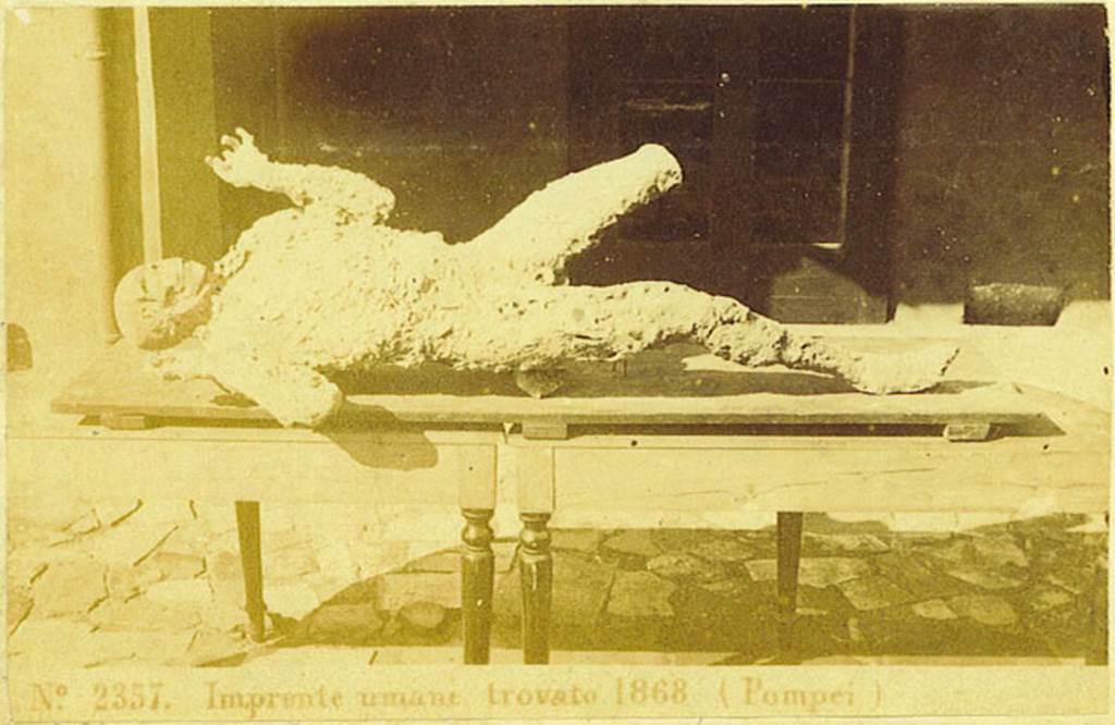 Photograph of the human plaster-cast found on 12th March 1868, in VII.2.16 Pompeii. 
Photo courtesy of Rick Bauer. This cast, known as the Fifth Victim, was placed in the Archaeological School, and it was here that Ernest Breton saw it, and described
This unfortunate was discovered lying on his stomach in a room to the left of the atrium of the House of Gavius Rufus.  Six other skeletons were near him from Breton, 1869.
See Dwyer, E., 2010. Pompeiis Living Statues. Ann Arbor: Univ of Michigan Press. (p. 80)
See Breton, Ernest. 1870. Pompeia, Guide de visite a Pompei, 3rd ed. Paris, Guerin. 
According to Fiorelli  Sette scheletri umani furono trovati in questo luogo, uno dei quali bocconi ed in atto di supremo sforzo, per emettere il respiro soffocato dalle esalazioni vulcaniche, fu da ma rivestito delle forme del suo corpo, ricavandole dalla impronta che vi era rimasta nella cenere. See Fiorelli, G. (1875). Descrizione, (p.187).  See Pappalardo, U., 2001. La Descrizione di Pompei per Giuseppe Fiorelli (1875). Napoli: Massa Editore. (p.81)
(translation   Seven human skeletons were found in this place, one of which was face down and in the process of making his last effort to emit his breath choked by volcanic fumes.  He was clothed by me in his bodily forms by obtaining them from the impression that remained in the ashes.
