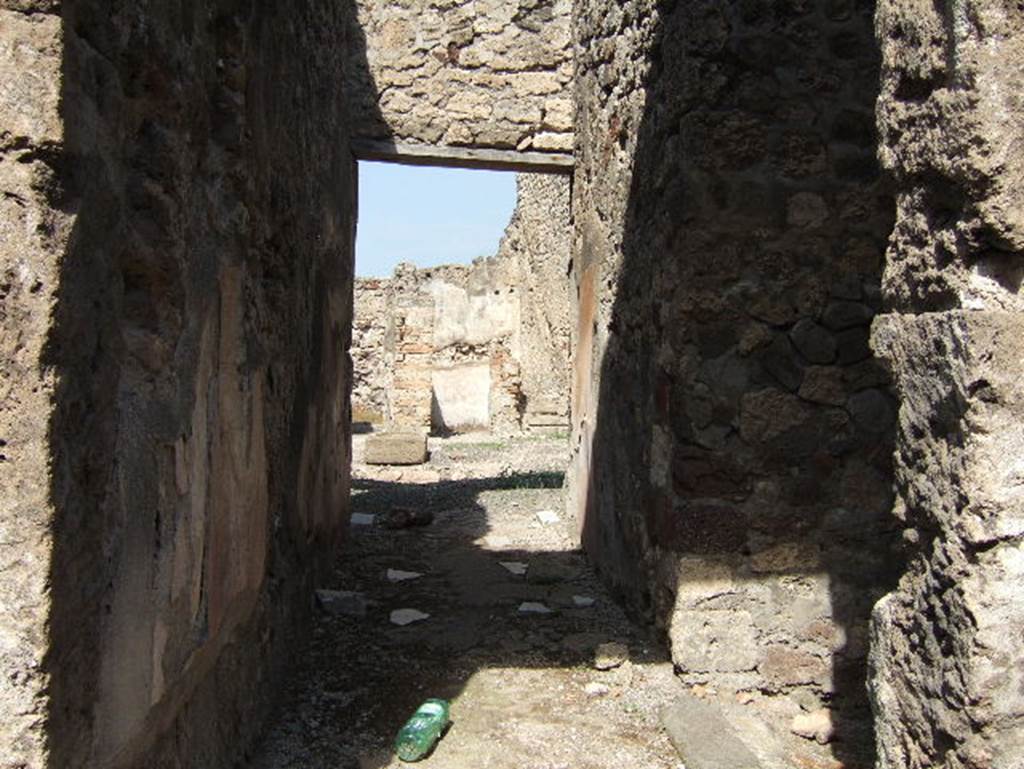 VII.15.3 Pompeii. September 2005. Looking north along entrance corridor to atrium.
Embedded into the cocciopesto flooring were tiles/slabs of marble leading to the atrium.  The zoccolo/dado/plinth of the walls was divided into panels imitating large marble slabs, whose veins were obtained with large white and black strokes.
The middle zone of the walls was simply painted in white. The doorway on the right leads to the latrine.
