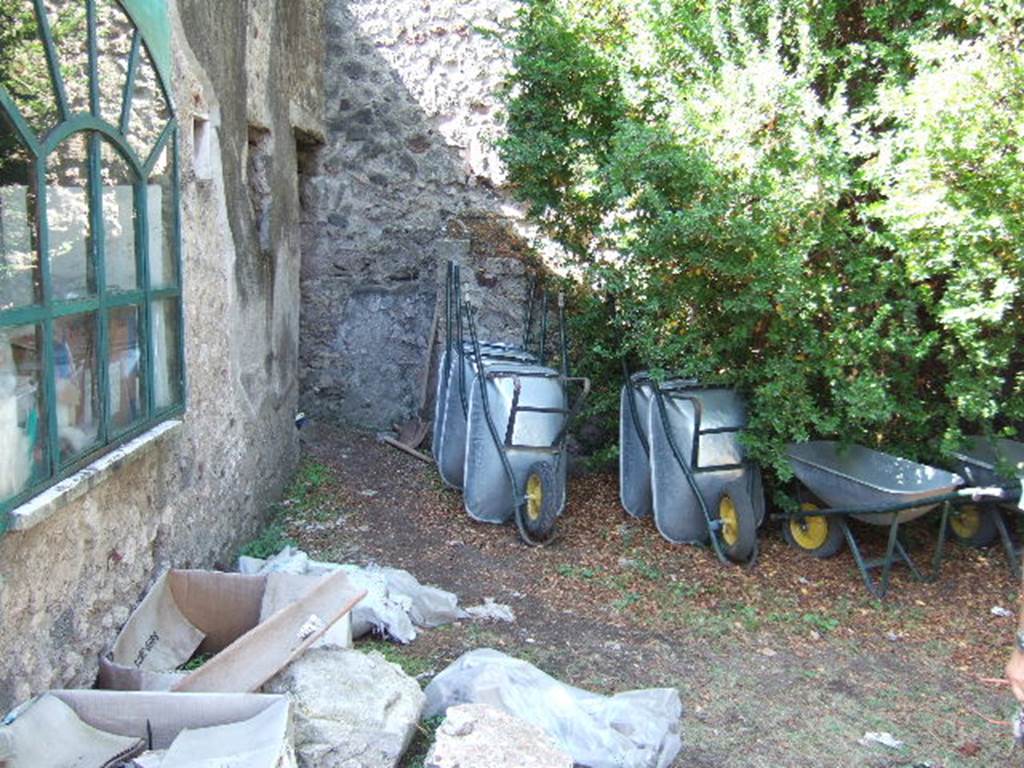 VIII.3.14 Pompeii. September 2005. West side of garden with doorway to small room or cupboard on west side of cubiculum. At the rear of the wheelbarrows are steps to an upper floor.
