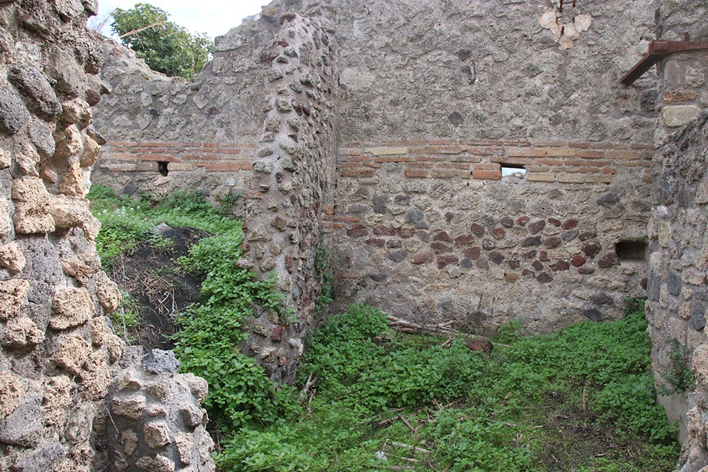 IX.7.16 Pompeii. October 2024. 
Room “d”, on south side of room 3, on right, looking south. On the left would be a doorway into room 6. Photo courtesy of Klaus Heese.

According to Boyce –
“In the kitchen, which is entered through the first room on the right of the atrium, on the north wall to the right of the entrance and on the west wall, is the lararium painting (h.1.50, w. on north wall 0.60, on the west wall 1.94): on the right of an altar stands the Genius in the usual attire, pouring a libation from a patera; on the left is the lower part of the figure of the tibicen and behind him stands a camillus wearing white tunic and carrying in his left hand, a shallow dish, taeniae in the right hand. Behind the Genius the popa, wearing a crown of leaves, holds a knife to the throat of a hog adorned with a red band around its belly. On each side of this group of four is a Lar in the usual attire. In the lower zone two yellow serpents, each with red crest, are confronted at an altar. The painting thus described is all on the west wall of the room. On the north wall are painted the following kitchen objects (from top to bottom): a hearth, an uncertain object – perhaps the fire-wood for the hearth – a hog’s head, a pot on a fire.
Traces of the older lararium painting, not entirely covered over by the later, are to be seen on the west wall, where the figure of a Lar can be made out on the left side.”
See Boyce G. K., 1937. Corpus of the Lararia of Pompeii. Rome: MAAR 14. (p. 87, no. 436) 
and Boyce gives the reference Bullettino dell’Instituto di Corrispondenza Archeologica (DAIR), 1883, 145. 

