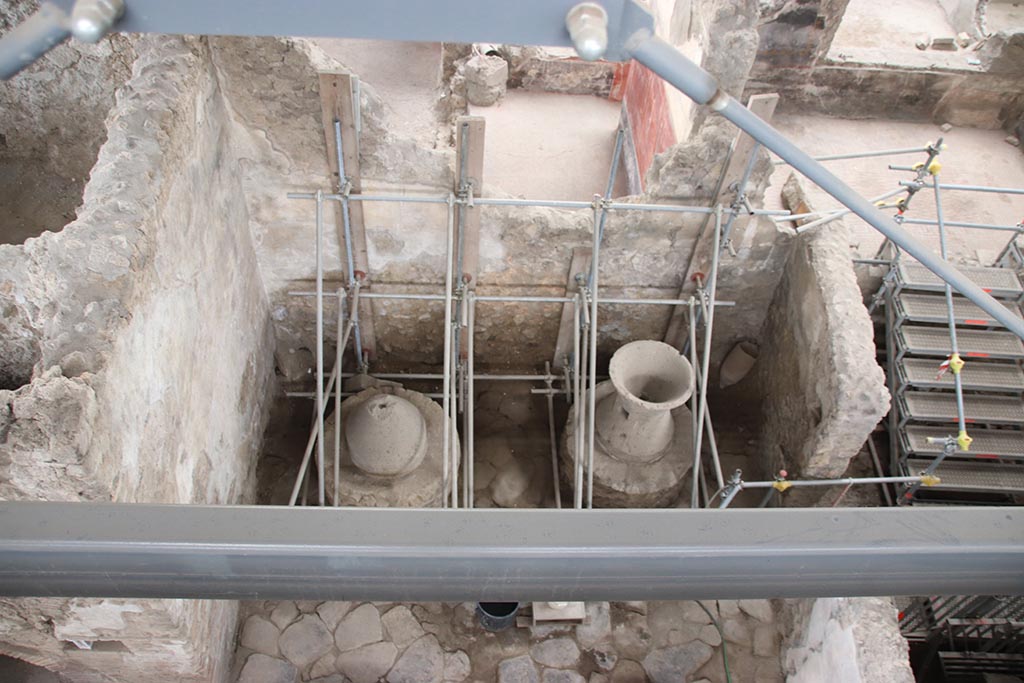 IX.12.6 Pompeii. October 2024. Room “f”, looking west on north side of oven “d” with two mill bases. Photo courtesy of Klaus Heese.