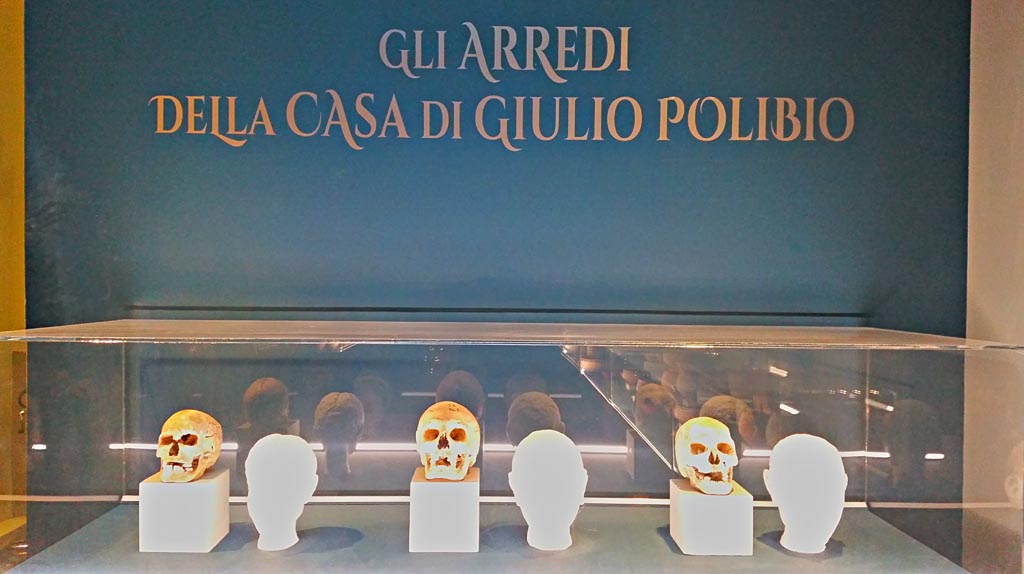 IX.13.1-3 Pompeii. December 2019. Room 10, heads of skeletons found in house, and their reconstructed faces. 
From left to right, the face of a young girl of around 20 years in the last months of pregnancy at the time of the eruption; that of an adult male  between 25 and 35 years of age; and that of an old man of around 60 years.  Photo courtesy of Giuseppe Ciaramella.
(Photographed at an exhibition “The furnishings of the House of Julius Polybius” (Guilio Polibio)).
