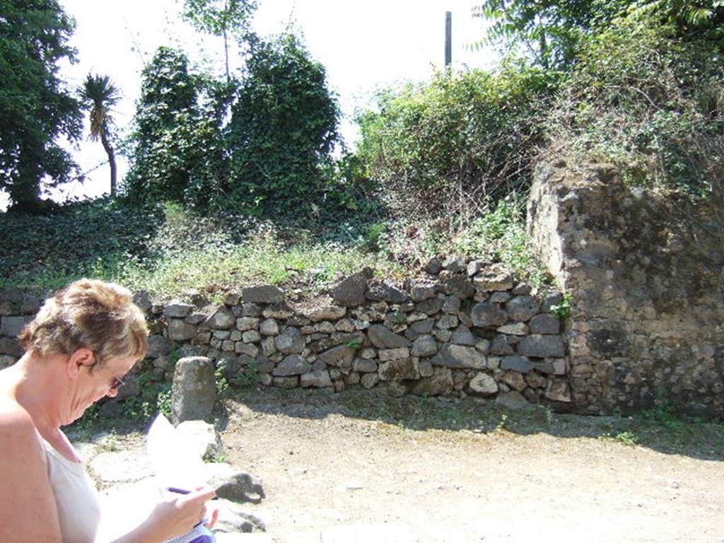 HGW06 Pompeii. May 2006. North side of entrance. According to Spano, found immediately to the left of the shop numbered 7, was a large block of material. This was found during a small excavation in the area, and can be seen on the right of the above photo. This large square mass of material contained a large circular basin, open above. This must have collected in the rain water which flowed from the high part of the Villa of Cicero, at the rear.
This basin, which had already been drawn by Mazois, was only entirely emptied of its eruptive material by this excavation. Finished with sturdy opus signinum, it was formed by an empty cylinder (1.90m deep, and 2.65m wide).The base was rather concave, and in it (to the south-east) was a distribution channel for the water.See Spano in Notizie degli Scavi, 1910, p.268-9.
