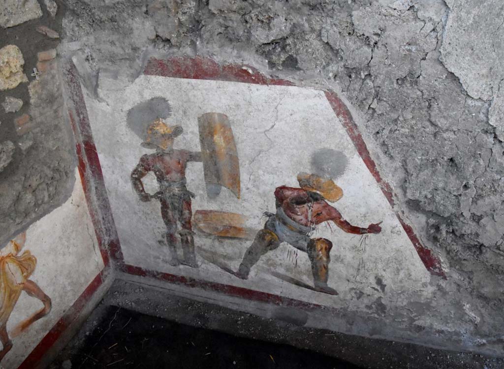 Two gladiators at the end of the fight, one wins the other succumbs.
The fresco of about 1.12 meters x 1.5 meters, found in a room behind the widening of the intersection of the Vicolo dei Balconi and the Vicolo delle Nozze D’Argento, has a trapezoidal shape, as it was located in the basement, perhaps of a shop. Above the painting we can see the imprint of the wooden staircase. 

It is very likely that this place was frequented by gladiators, it is in the Regio V, not far from the caserma dei gladiatori from where, among other things, come the highest number of graffiti inscriptions related to their world. In this gladiatorial fresco of a Murmillo and a Thracian, of particular interest is the extremely realistic representation of the wounds, such as that on the wrist and chest of the succumbing gladiator, which let out the blood that also bathes the legs.  We don't know what the final outcome of this fight was. You could die or have grace. In this case there is a singular gesture that the wounded Thracian makes with the hand, perhaps, to plead for salvation; it is the gesture of ad locutia, usually made by the emperor or the general to grant grace.

Due gladiatori al termine del combattimento, l’uno vince l’altro soccombe
L’affresco di circa 1,12 mt x 1,5mt, rinvenuto in un ambiente alle spalle dello slargo di incrocio tra il Vicolo dei Balconi e il vicolo delle Nozze d’Argento, ha forma trapezoidale, in quanto era collocato nel sottoscala, forse di una bottega. Si intravede al di sopra della pittura, l’impronta della scala lignea.

E’ molto probabile che questo luogo fosse frequentato da gladiatori. Siamo nella Regio V, non lontani dalla caserma dei gladiatori da dove, tra l’altro, provengono il numero più alto di iscrizioni graffite riferite a questo mondo. In questo affresco di un Mirmillone e un Trace, di particolare interesse è la rappresentazione estremamente realistica delle ferite, come quella al polso e al petto del gladiatore soccombente, che lascia fuoriuscire il sangue e bagna i gambali.  Non sappiamo quale fosse l’esito finale di questo combattimento. Si poteva morire o avere la grazia. In questo caso c’è un gesto singolare che il trace ferito fa con la mano, forse, per implorare salvezza; è il gesto di ad locutia, abitualmente fatto dall’imperatore o dal generale per concedere la grazia.
http://pompeiisites.org/comunicati/laffresco-dei-gladiatori-combattenti-nuova-scoperta-nella-regio-v/
