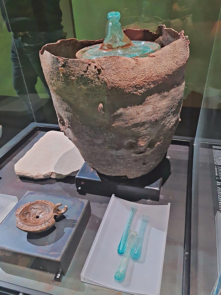 Porta Sarno la tomba di Marcus Venerius Secundio. Tomb of Novia Amabiles. March 2024.
A terracotta lamp, a bronze nail, a marble slab and glass unguentaria and a bronze coin were also found.
Photo courtesy of Giuseppe Ciaramella.
On display in exhibition in Palaestra entitled – “L’altra Pompei, vite comuni all’ombra del Vesuvio”. March 2024.
