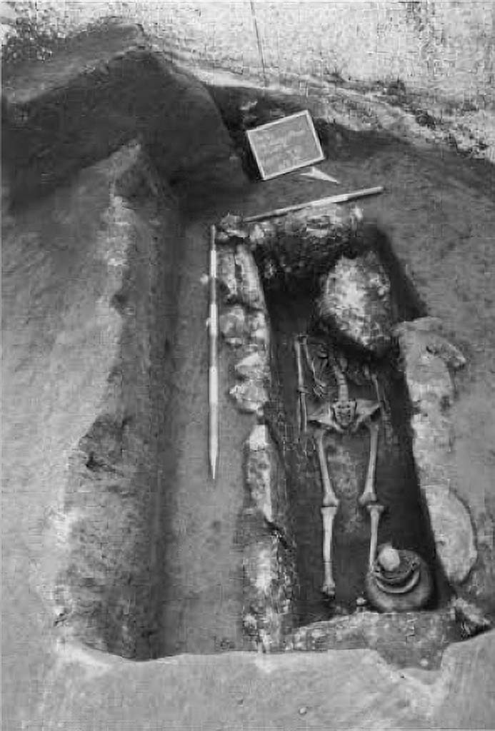 Pompeii Porta Sarno Necropolis. 1999.
Skeleton in inhumation tomb from the Samnite period, encased in travertine blocks.
The first tomb explored contained a single skeleton with the head to the west. At the feet were the grave goods, consisting of an achromatic olla, a black varnished kylix, stamped with 6 rosettes joined by circular arcs, a black varnished oinochoe, with a round mouth. They are, as can be seen, poor burials dating back to between the mid-4th and the beginning of the 3rd century a. C. 

Scheletro in tomba ad inumazione di età sannitica, a cassa di blocchi di travertino.
La prima tomba esplorata conteneva un solo scheletro con testa ad ovest. Presso i piedi era il corredo, costituito da un'olla acroma, una kylix a vernice nera, con stampigliatura a 6 rosette congiunte da archi di cerchio, una oinochoe a vernice nera, con bocca rotonda. Sono, come si vede, sepolture povere databili tra la metà del IV e gli inizi del sec. III a. C. 

See/Vedi Suburbio Orientale in Rivista di Studi Pompeiani X, 1999, p. 180, fig. 1.
