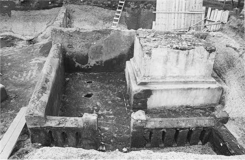 Pompeii Porta Sarno Necropolis. 1999. Podium tomb A. Funerary site with a monument on podium and enclosure.

In 1999 a new necropolis area was also discovered in which, in particular, is a large funerary monument - of the "a dado" (cube) type on a podium - of which, unfortunately, the upper part has been lost with it the epigraph that probably must have been there, so that the owner remains unknown. The building, in opus incerta, with corners in brick work, covered with white plaster, is contained in an enclosure in opus incerta work, in which narrow vertical windows open. At the base of the rear side, there is a niche, in turn containing a smaller niche in which a columella with the related cinerary material was placed, stuck in the ground. In the space between the enclosure and the podium, cavities relevant to the roots of trees, probably cypresses, that surrounded the monument were highlighted.

Nel 1999 è stata, inoltre, scoperta una nuova area di necropoli nella quale è da segnalare, in particolare, un grande monumento funerario - del tipo "a dado" su podio - del quale, purtroppo è andata perduta la parte superiore e con essa l'epigrafe che, verosimilmente, doveva esserci, così che ne resta sconosciuto il proprietario. L'edificio, in opera incerta, con ammorsature angolari in opera laterizia, rivestito di intonaco bianco, è inserito in un recinto in opera incerta, nel quale si aprono strette afinestrature verticali. Alla base del lato posteriore, si apre una nicchia, a sua volta contenente una nicchia più piccola nella quale era posta, infissa nel terreno, una columella con il cinerario relativo. Nello spazio tra il recinto e il podio, sono state evidenziate cavità pertinenti alle radici di alberi, probabilmente cipressi, che circondavano il monumento.

See/Vedi Suburbio Orientale in Rivista di Studi Pompeiani X, 1999, p. 181, fig. 2.
