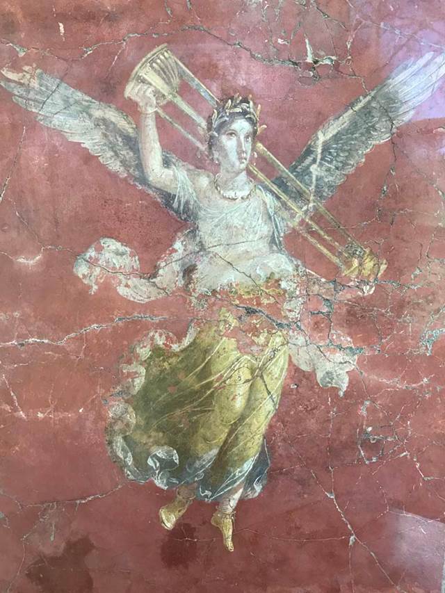 Complesso dei triclini in località Moregine a Pompei. April 2019. Triclinium C, east wall.
Vittoria con tripode. Vittoria with tripod, on display in Pompeii Palaestra.
Vittoria alata con gli attributi di Apollo. Winged Victory with the attributes of Apollo.
This is shown on the east wall of triclinium C but may have come from Triclinium D or E.
According to Mario Pagano, the difference in the background colour, red in this case, [triclinium D has black background colour] gives rise to the suspicion that this Winged Victory does not belong, as shown by the confused documentation, to the destination of triclinium D, but to that of the adjacent triclinium [E?], of which there is no recovery of the pictorial decoration.
See Guzzo, P., (A Cura di), 1997. Pompeii: Picta Fragmenta. Torino: Umberto Allemandi, p. 149 no. 116.
Photo courtesy of Rick Bauer.
