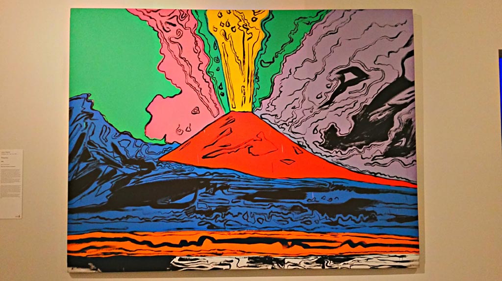 Vesuvius, acrylic on screen, painted by Andy Warhol (Pittsburgh, 1928 – New York, 1987), in 1985.
On display in exhibition “Pompei e Santorini” in Rome, 2019. Photo courtesy of Giuseppe Ciaramella.
According to the information card –
“In 1985, the Neapolitan art dealer Lucio Amelio organized a show of work by Andy Warhol in the Museo di Capodimonte entitled Vesuvius. 
For the occasion, the artist developed a Pop revisitation of the volcano in a series of screenprints whose bright colours alter the drama of the eruption in an unprecedented cartoon-like vision. Like many artists, Warhol fell under the sublime spell of Vesuvius, the best-known landmark of the Neapolitan landscape. As he wrote – “Vesuvius for me is something much greater than a myth. It is terribly real.”

