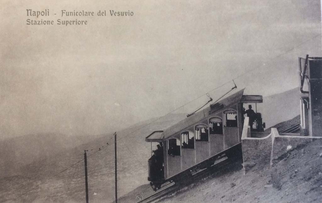 Postcard for Vesuvius Funicular, showing Upper Station. Not dated but must be between 1910 and 1944.
There is a handwritten note on rear – “The 1910 Funicular lasted until 1944”.  Photo courtesy of Rick Bauer.
After the 1906 eruption the funicular was out of action and reconstruction was only completed in 1909.
It reopened in 1910 with two new 5-bay end loading cars, numbered 1 and 2, which seated 16 with 8 standing. 
The car in this photo is car number 1.
The line now had overhead wire and the cars bow collectors to provide electric light, bell signals and a telephone. 
The funicular could now run an after dark service.
The funicular was permanently closed after being destroyed by the Vesuvius eruption of 1944.
